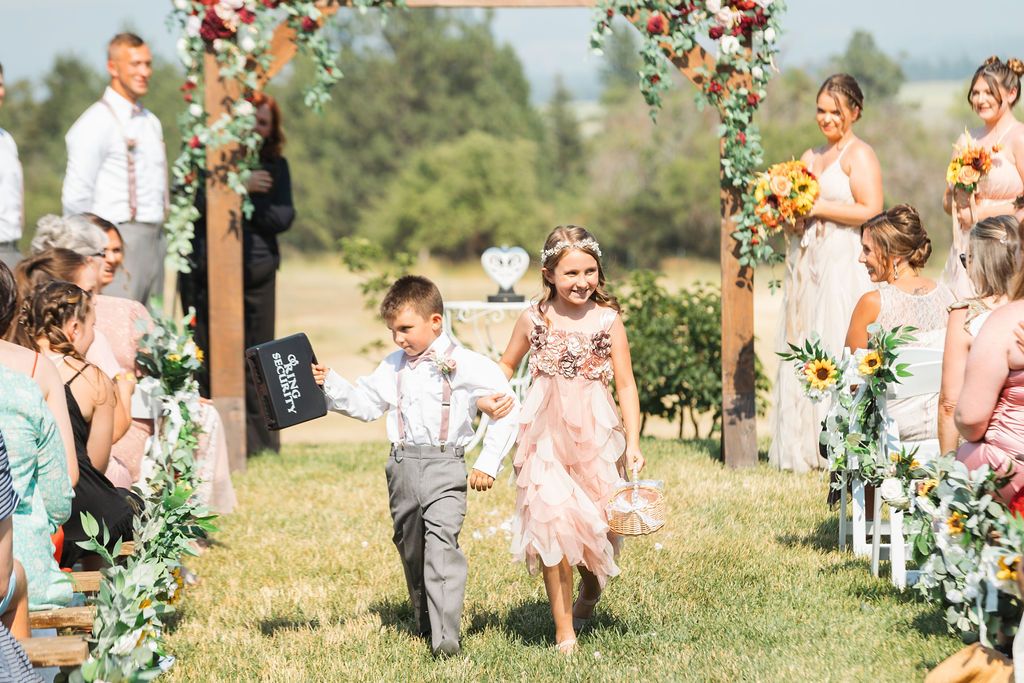 Wedding guests watch as the flower girl and ring bearer walk down the aisle at an outdoor wedding ceremony at Lavender Manor near Spokane WA